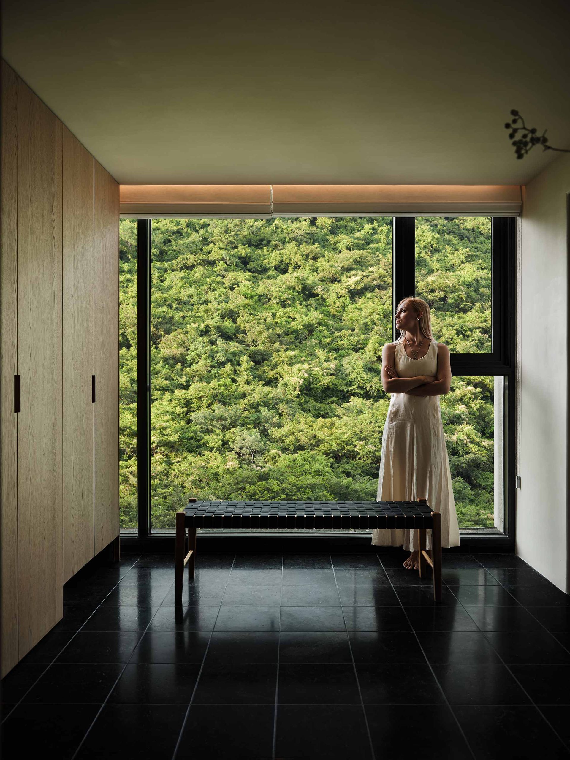现代极简卧室实景：左侧高柜与墙面一体，木纹门板配黑色竖向拉手，窗边长凳呼应整体调性